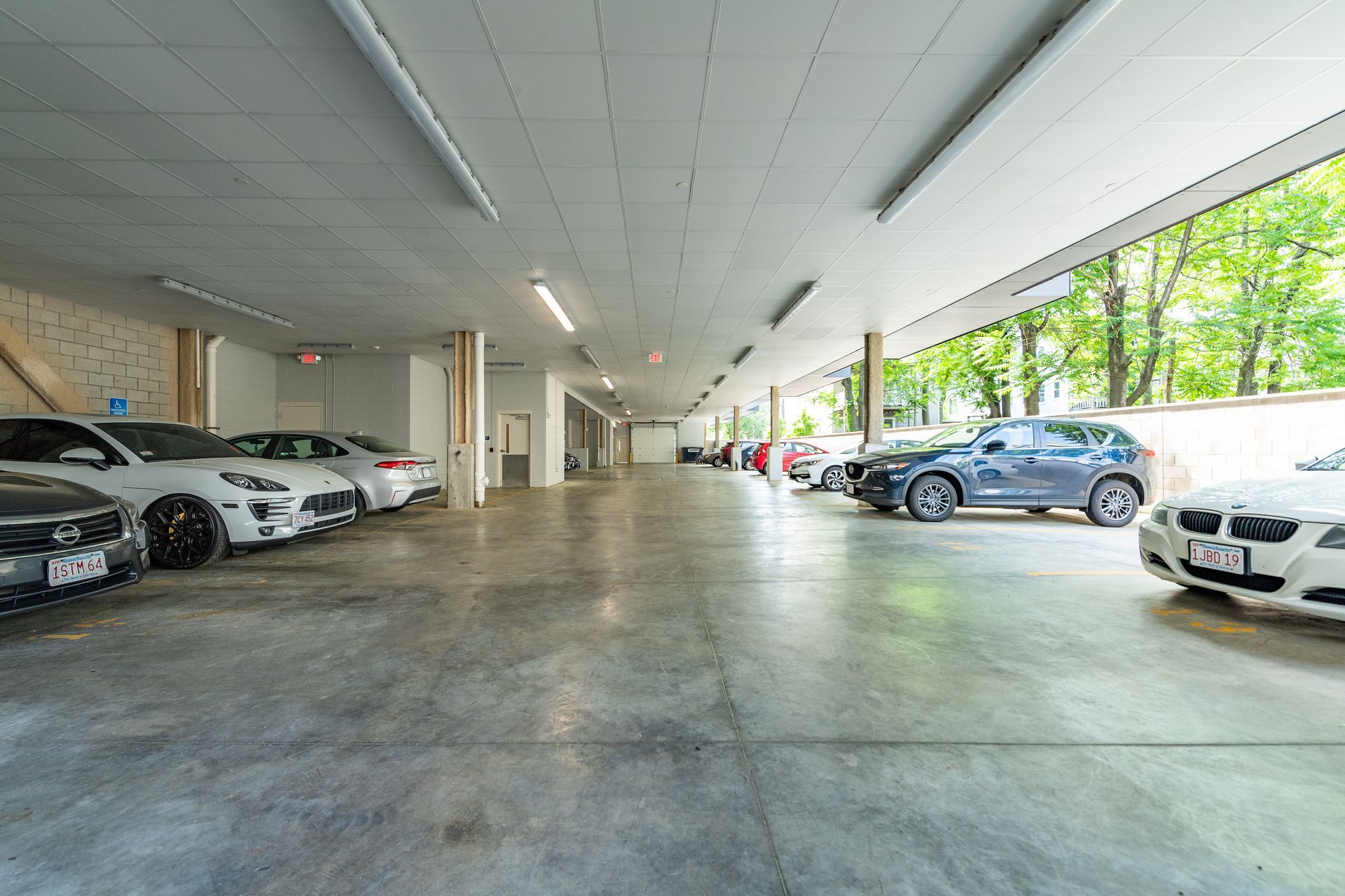 Cars parked in a long, covered parking garage with a concrete floor and bright overhead lights.
