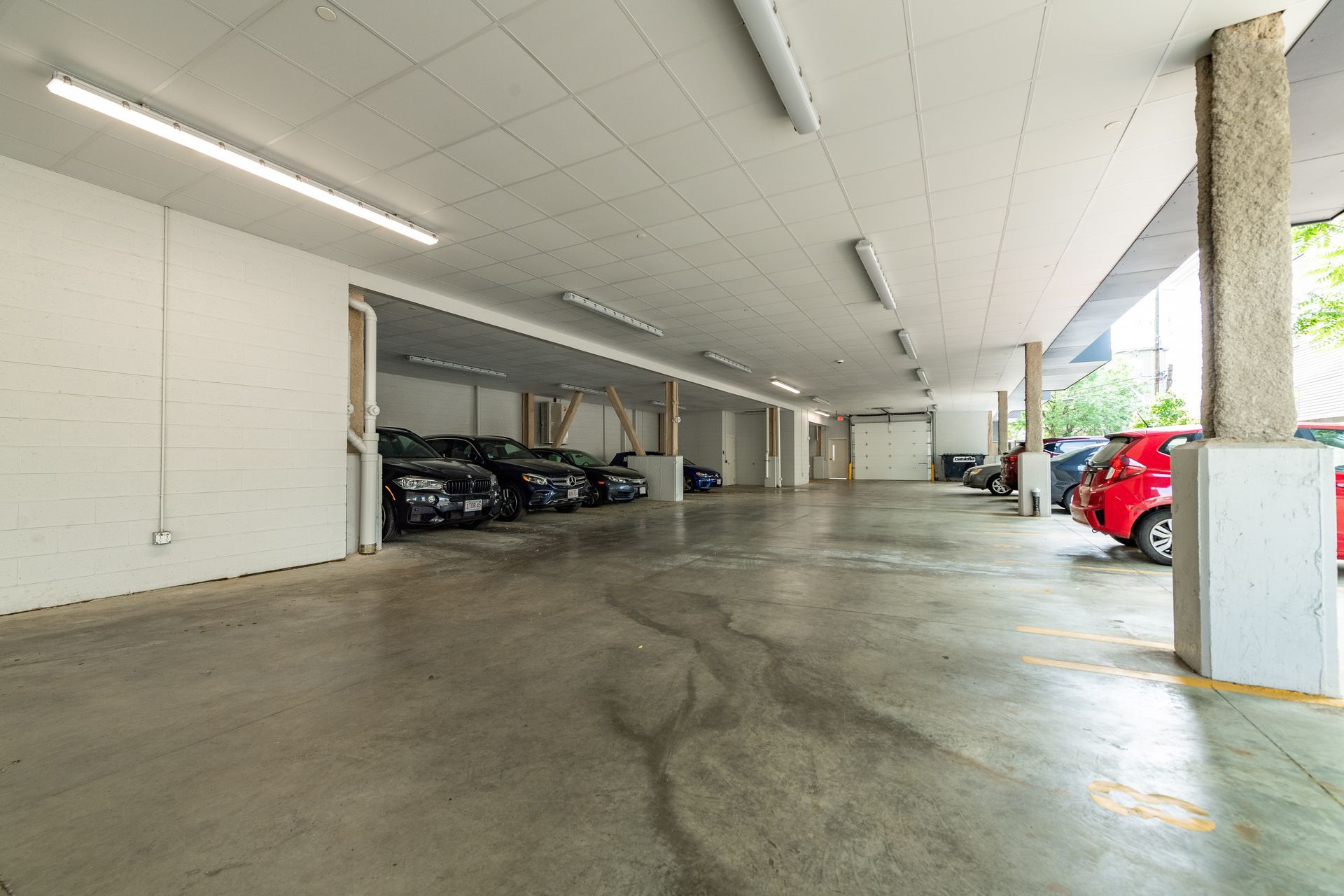 A covered parking garage with parked cars. Concrete floor, white walls and ceiling, and fluorescent lights.