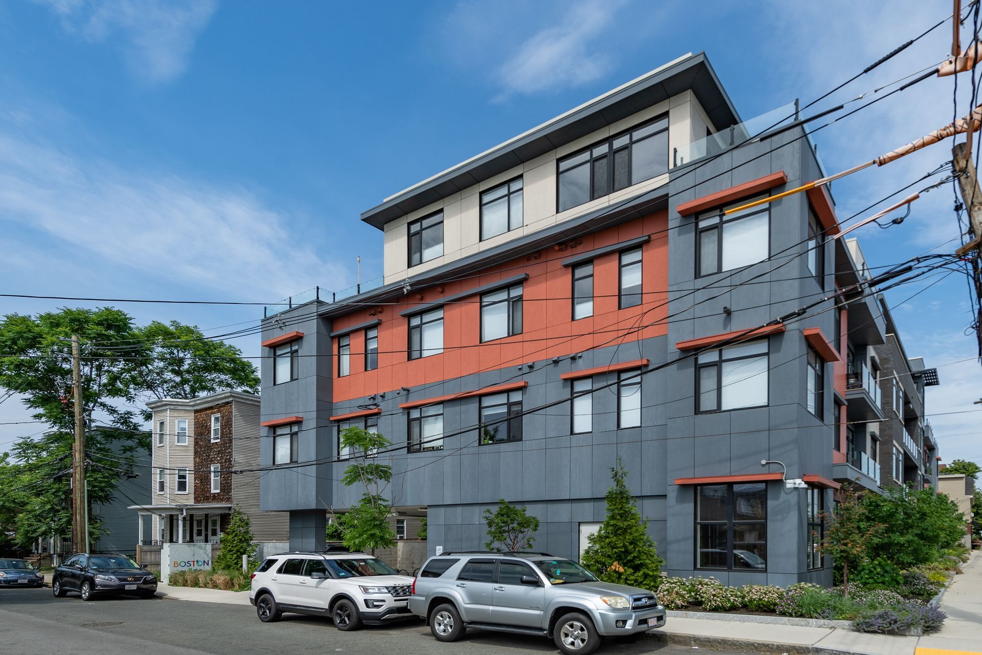 Modern gray and orange apartment building on a street with cars parked in front.