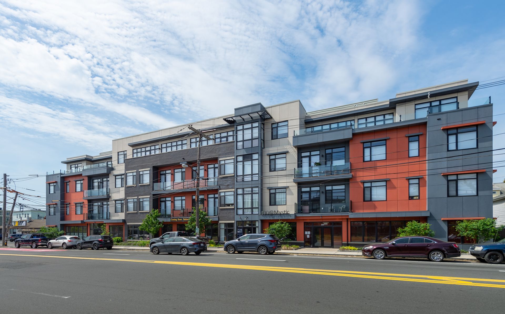 Multi-story modern building with orange and gray facade, cars parked in front under a blue sky.