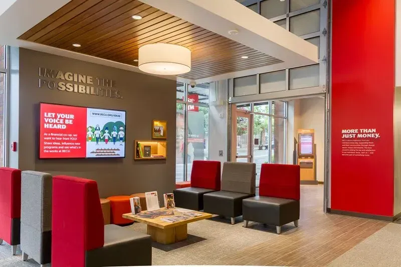 A waiting room with a table and chairs and a large screen on the wall.