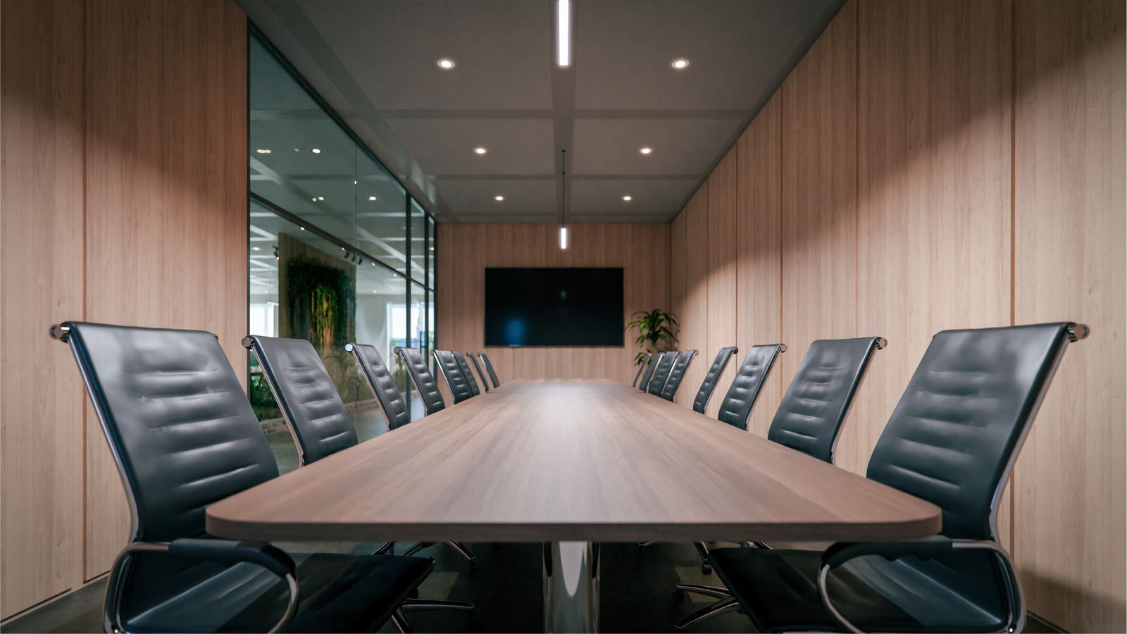 Meeting room with long table, black chairs, wood panel walls, and a large screen.