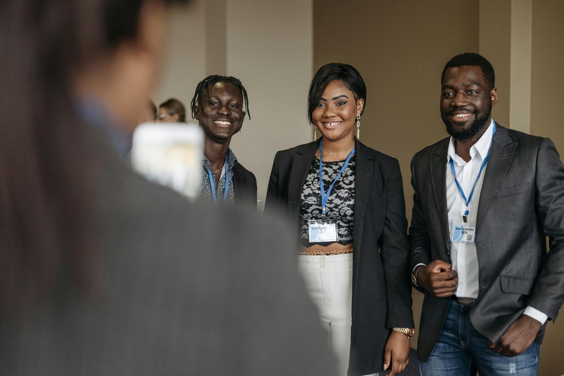 Three people with lanyards smiling; indoors, in a conference setting.