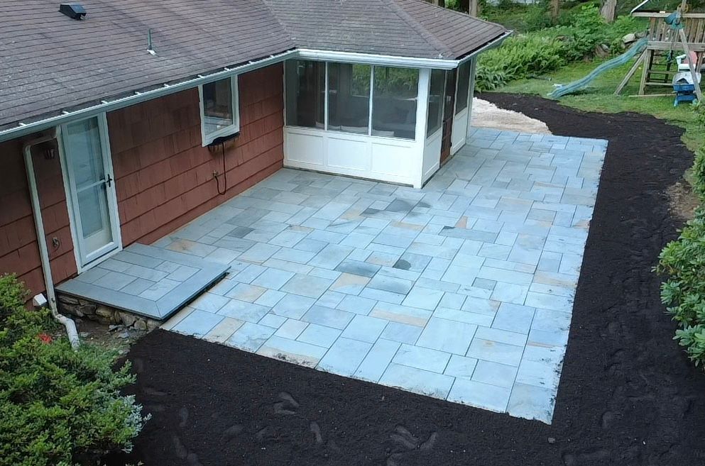 Backyard patio with blue stone pavers, a screened porch, and mulched landscaping.