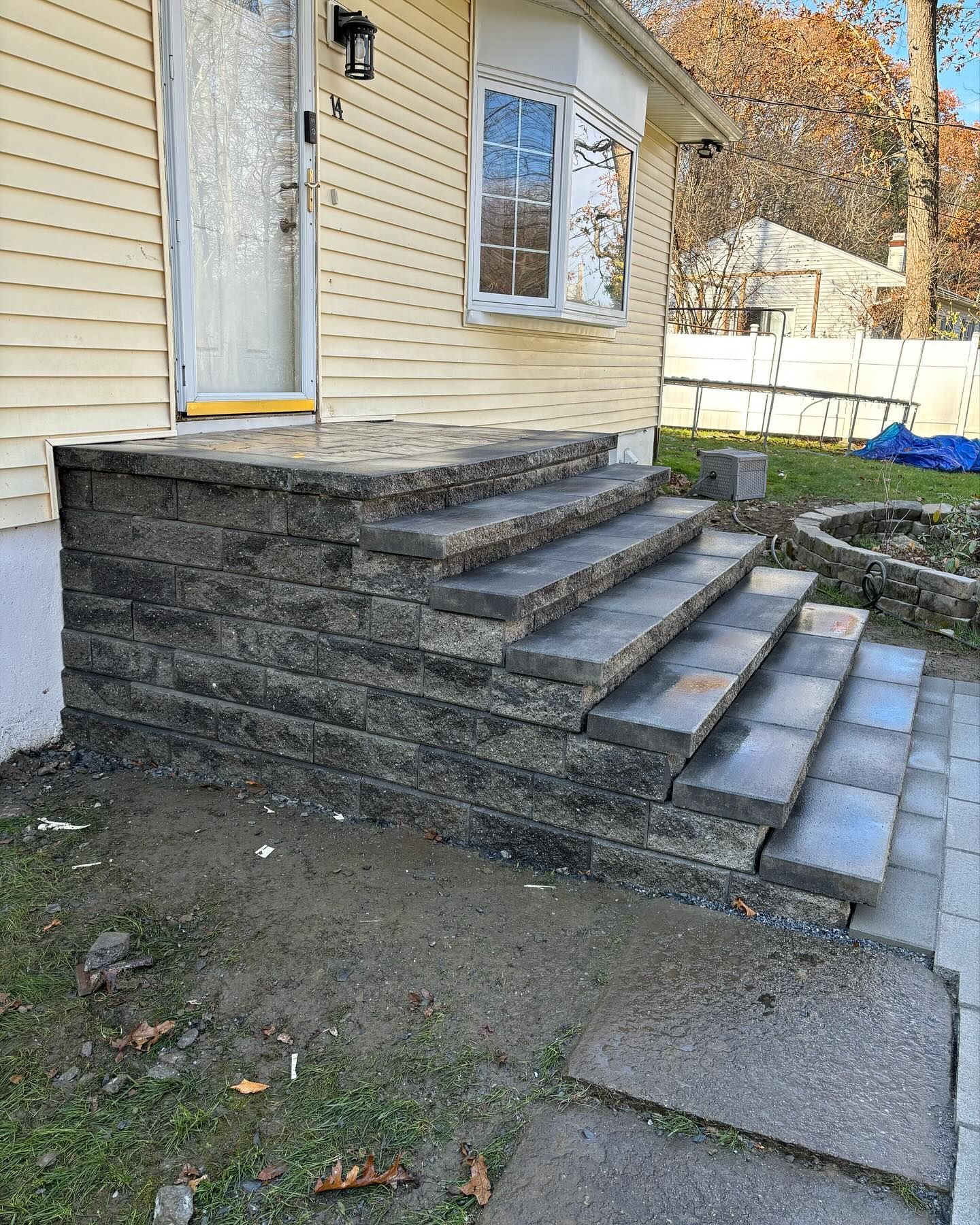 Stone steps leading up to the front door of a yellow house. The ground is dirt.