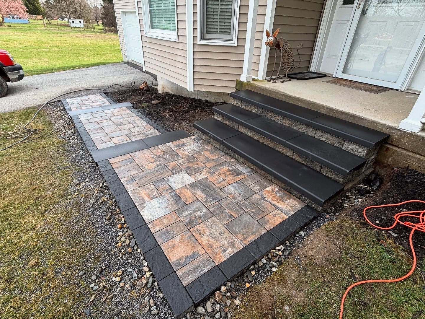 Brick pathway and steps leading to a house entrance. Pavers are bordered by dark blocks.