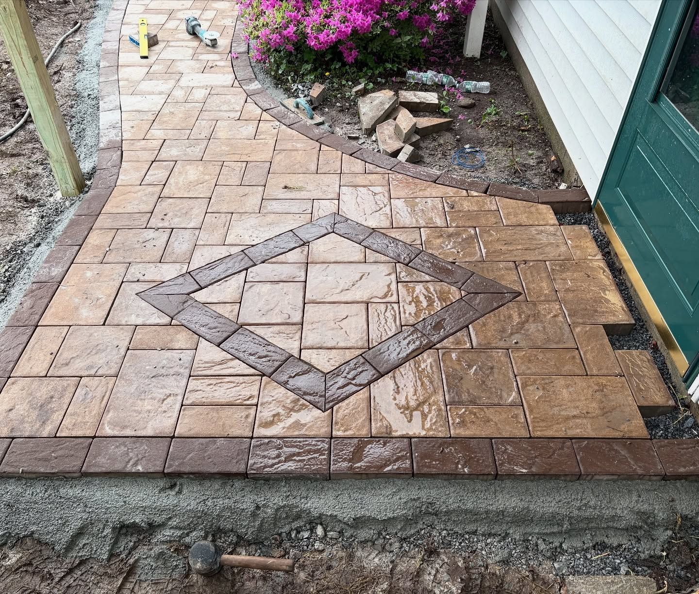 Brick patio with a diamond pattern, bordered by garden plants and a house wall