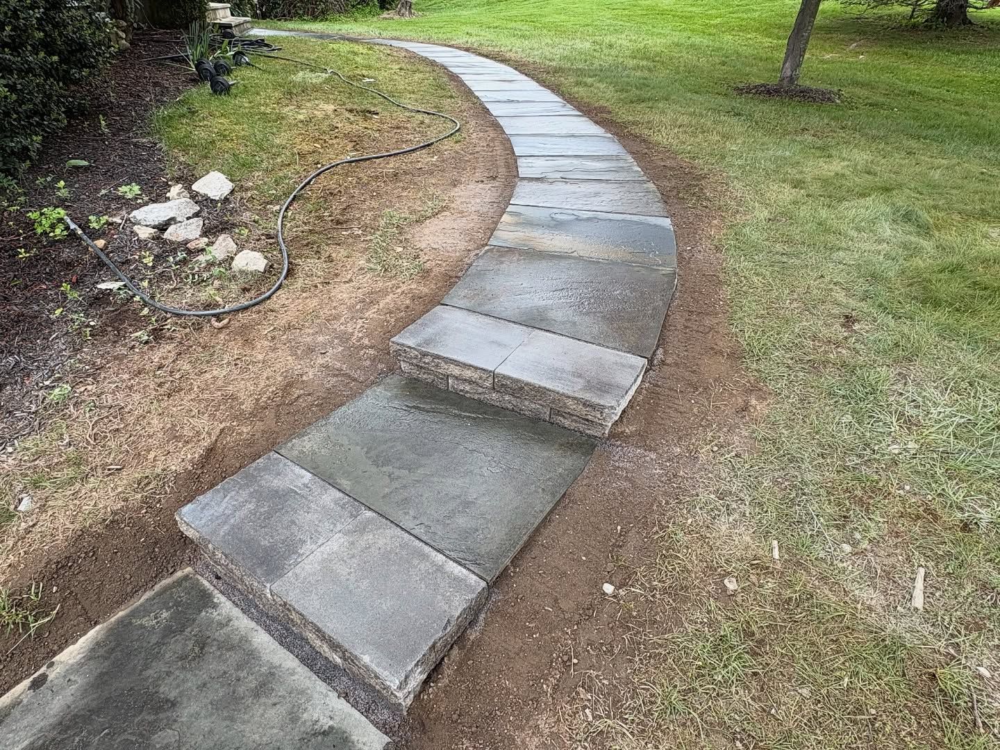 Stone walkway under construction, winding through a grassy yard.