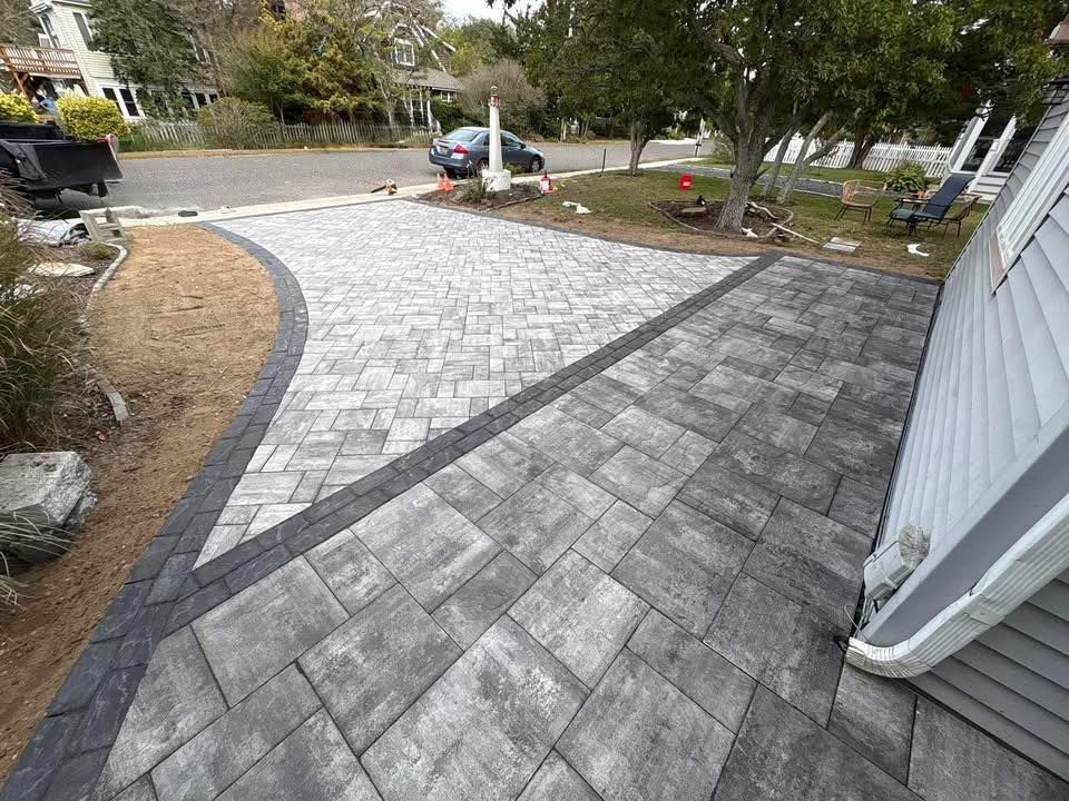 Driveway paved with gray and black rectangular pavers, with a contrasting stone border.