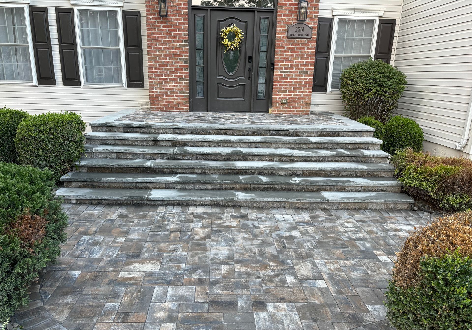 Stone steps leading to a front door with a brick facade and shrubs.