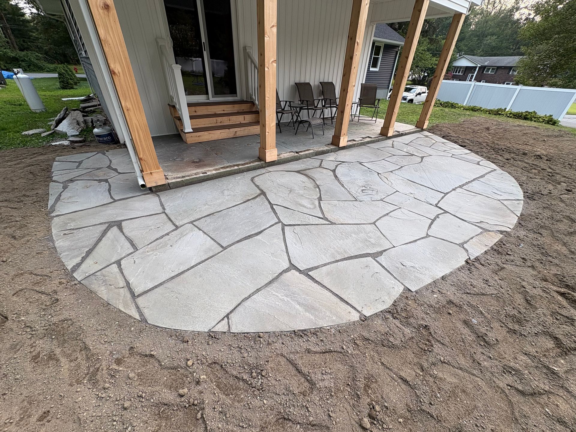 A patio made of irregular stones, adjacent to a house with a covered porch.