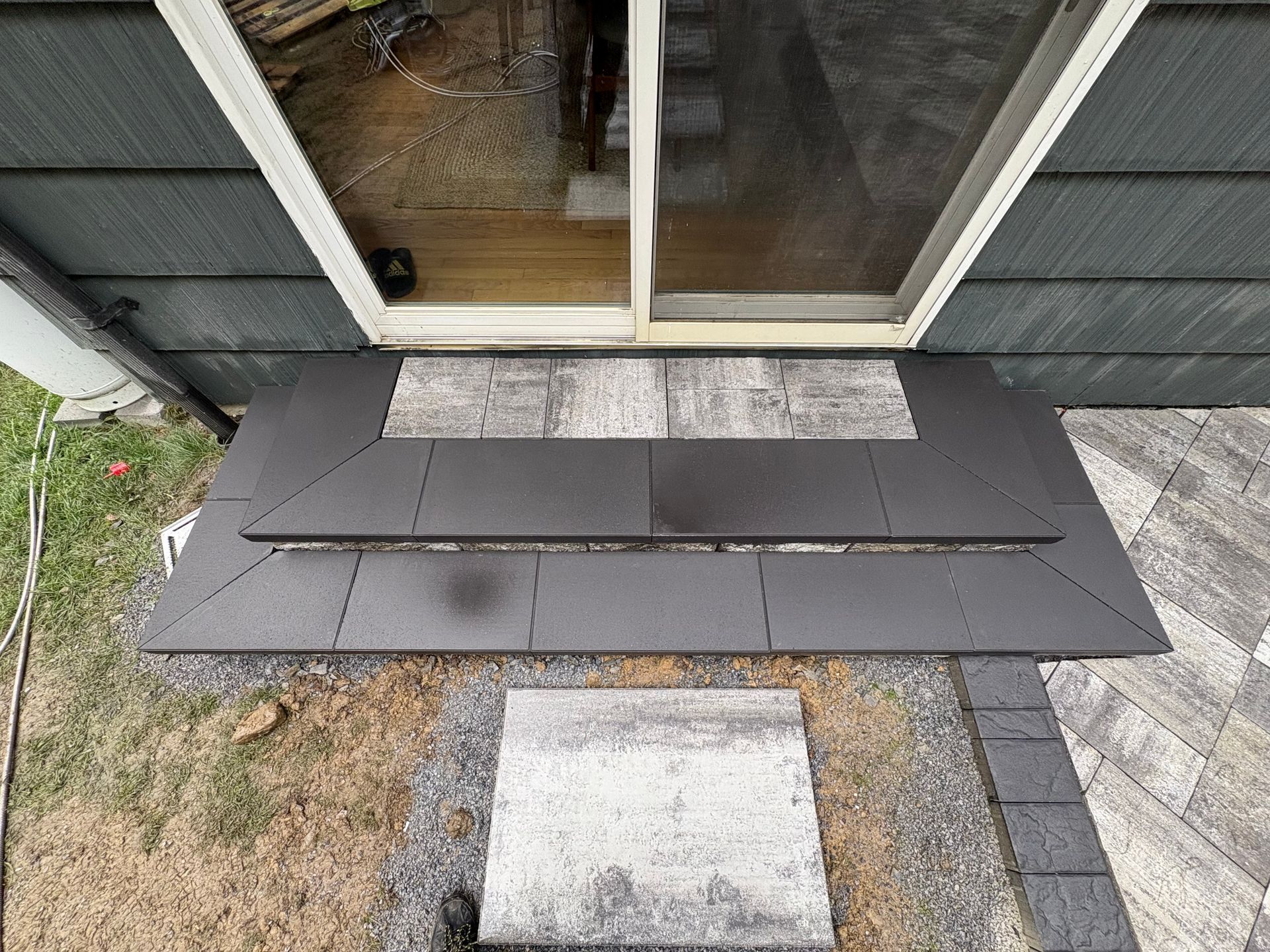 Dark gray tiles forming a patio in front of a glass door. Pavers and gravel surround.