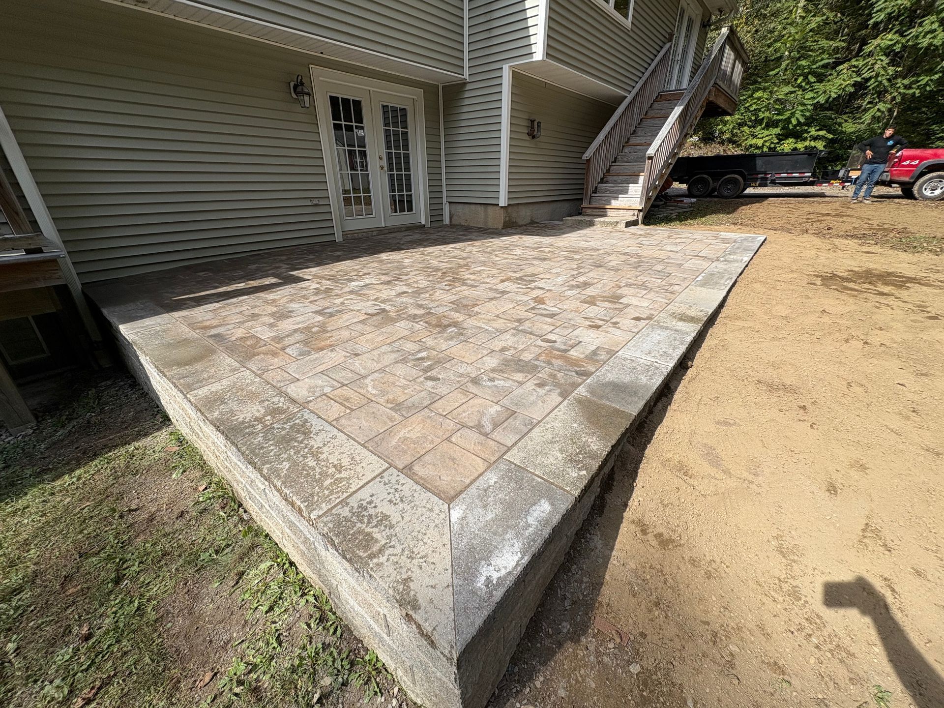 Brick patio with retaining wall next to a house with stairs.
