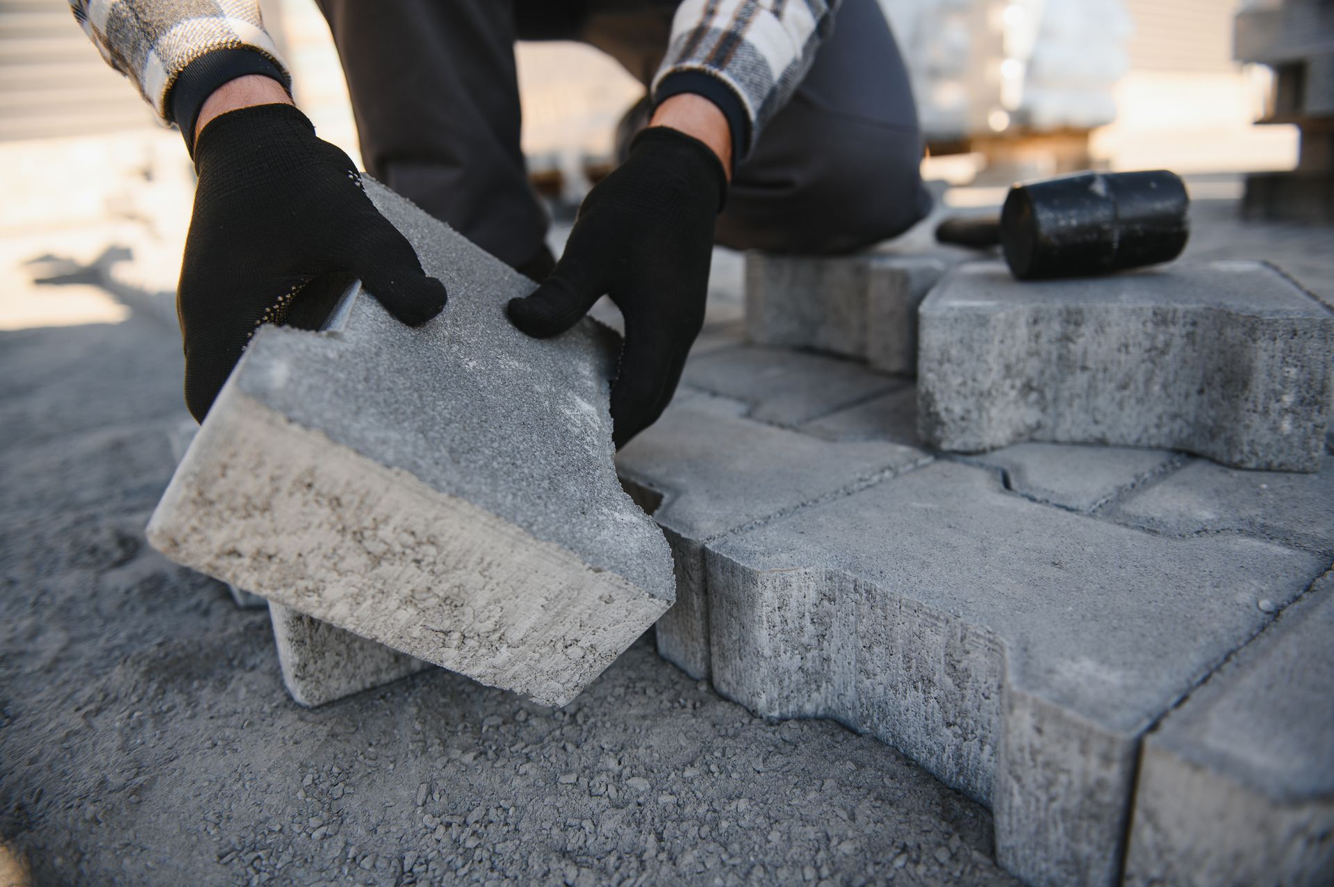 Gloved hands placing concrete pavers on a patio during outdoor paving work