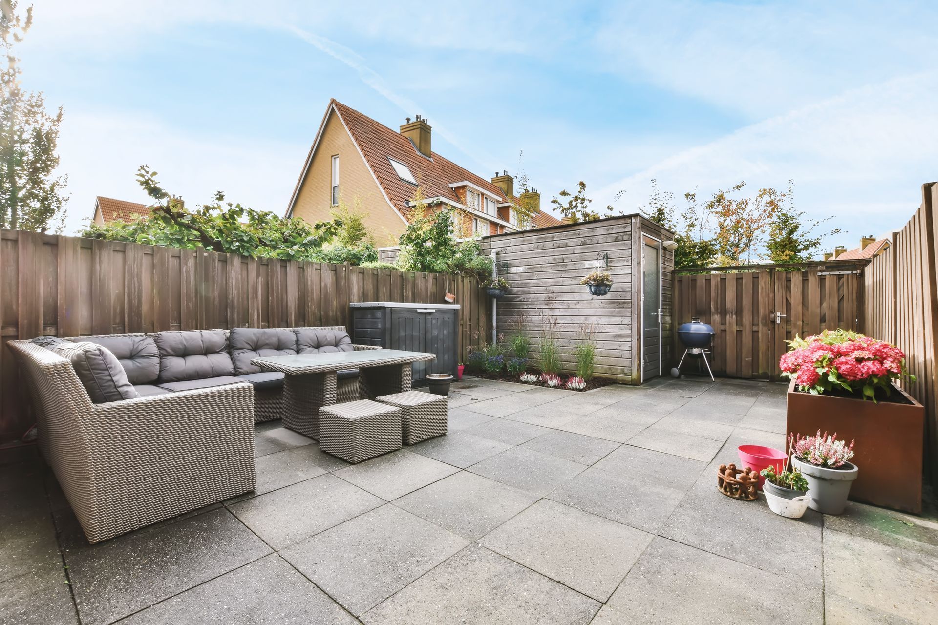 Backyard patio with wicker seating, square pavers, wooden fences, and potted flowers.