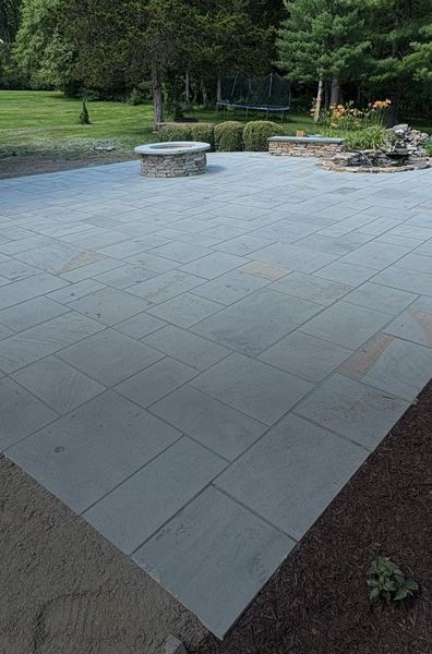 Large stone patio with fire pit and landscaping in backyard.