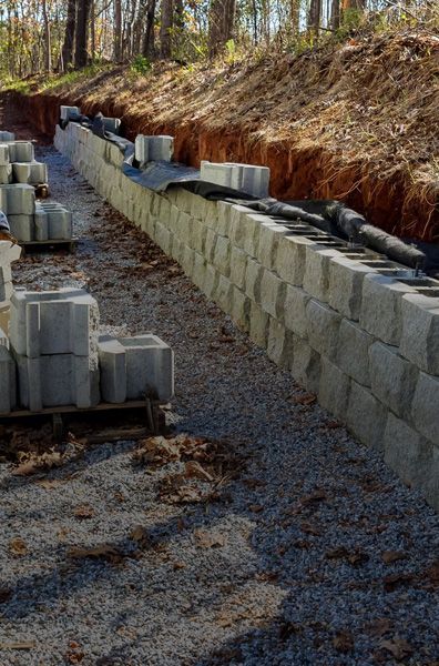 Retaining wall under construction with stacked concrete blocks and gravel base.