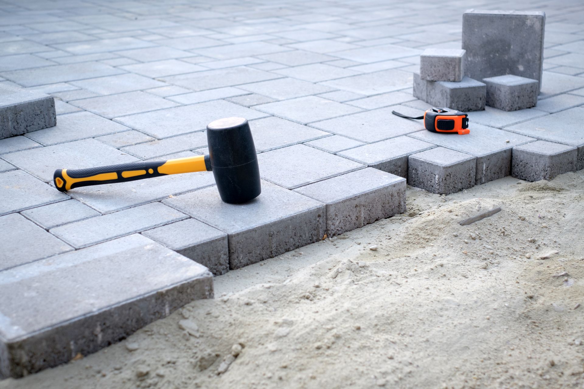 Paving stones and curb under construction, with a sledgehammer and tape measure on the sidewalk.