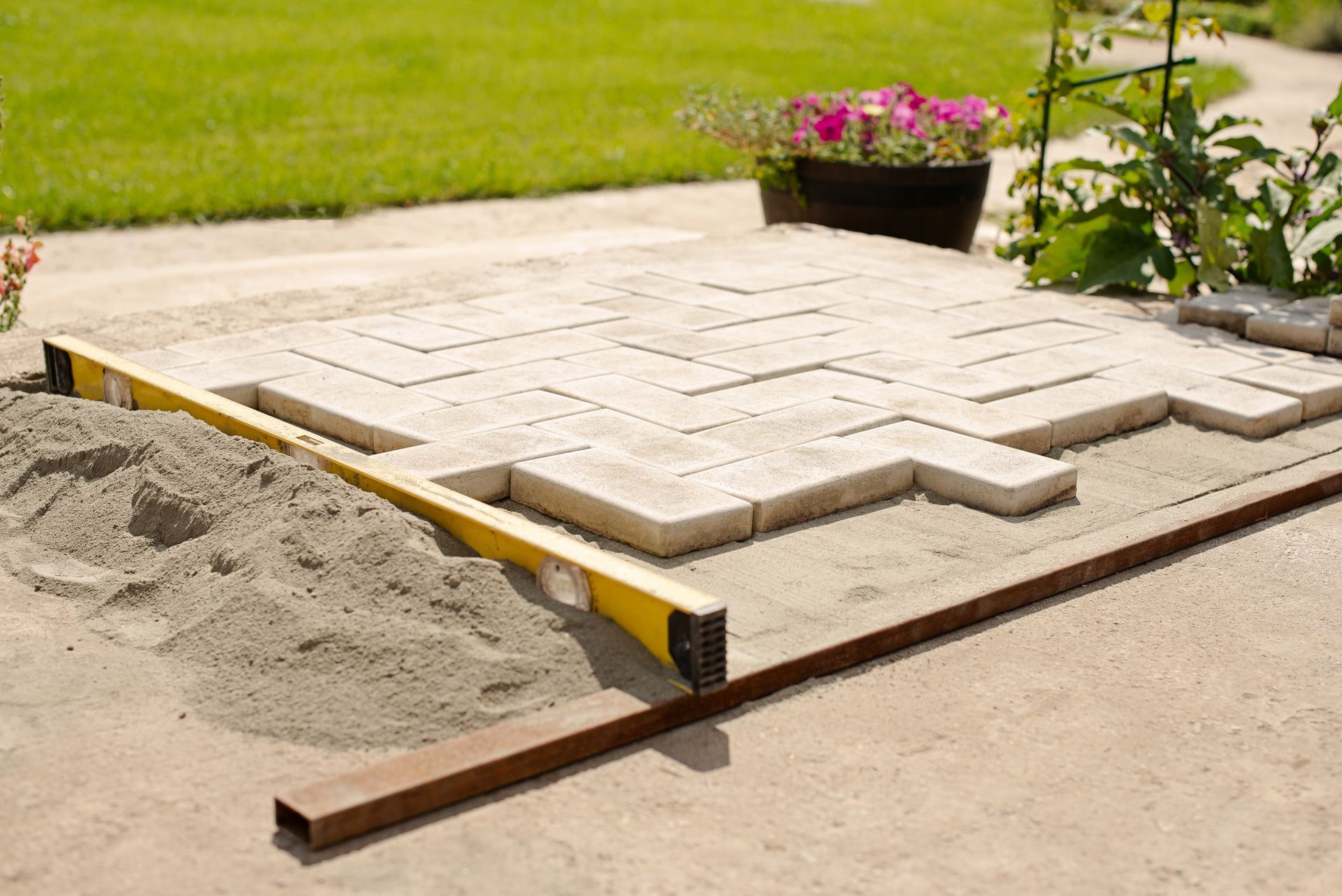 Patio pavers being laid beside a sand bed and garden flower pot on a lawn
