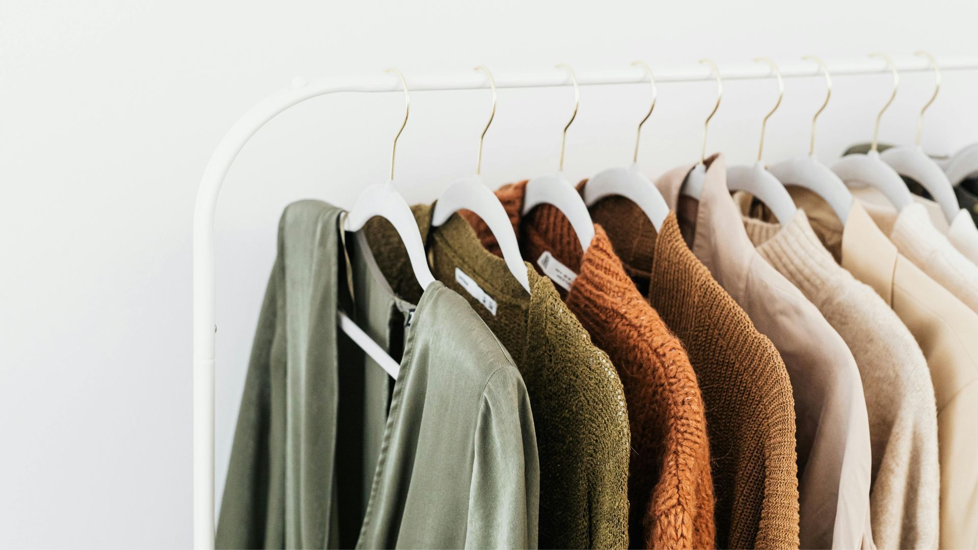 Clothing rack with an array of sweaters and shirts in a neutral color palette of green, brown, and cream.