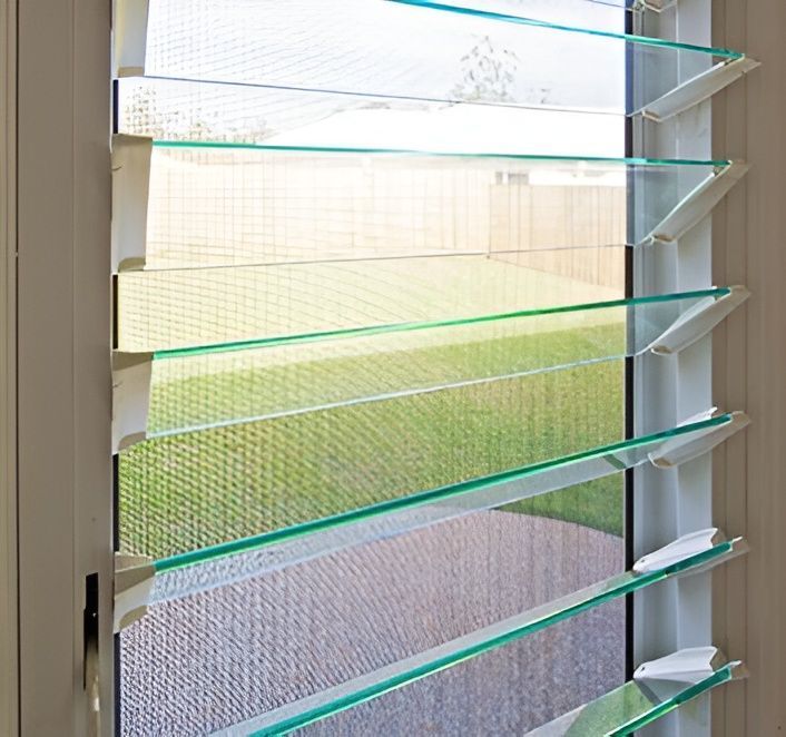 A close-up of a white window with multiple horizontal glass louvers, providing an adjustable view of a green lawn and sunny sky. — Maryborough Bay Glass & Aluminium in Maryborough, QLD