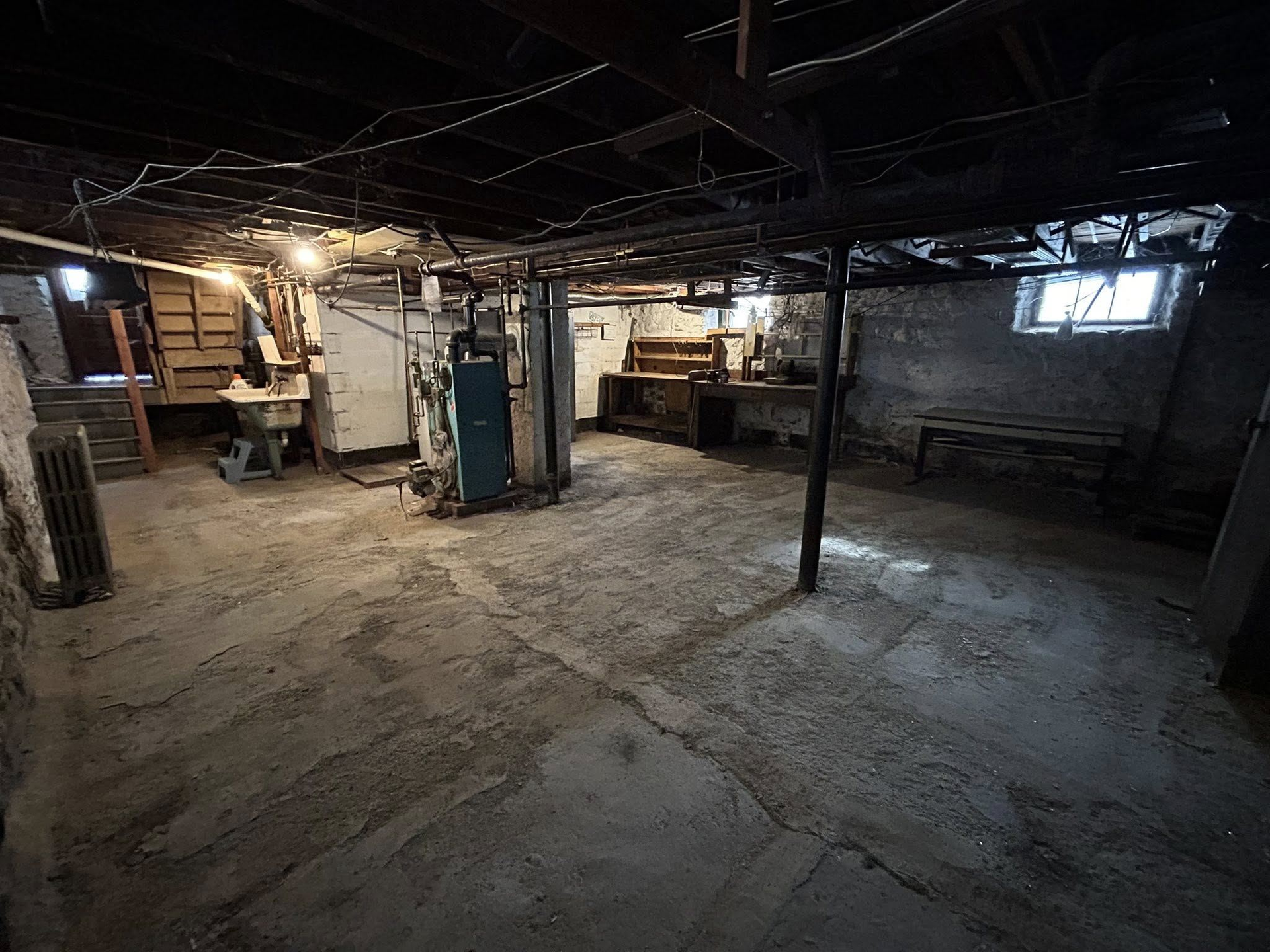 An empty basement with a blue boiler and a sink.