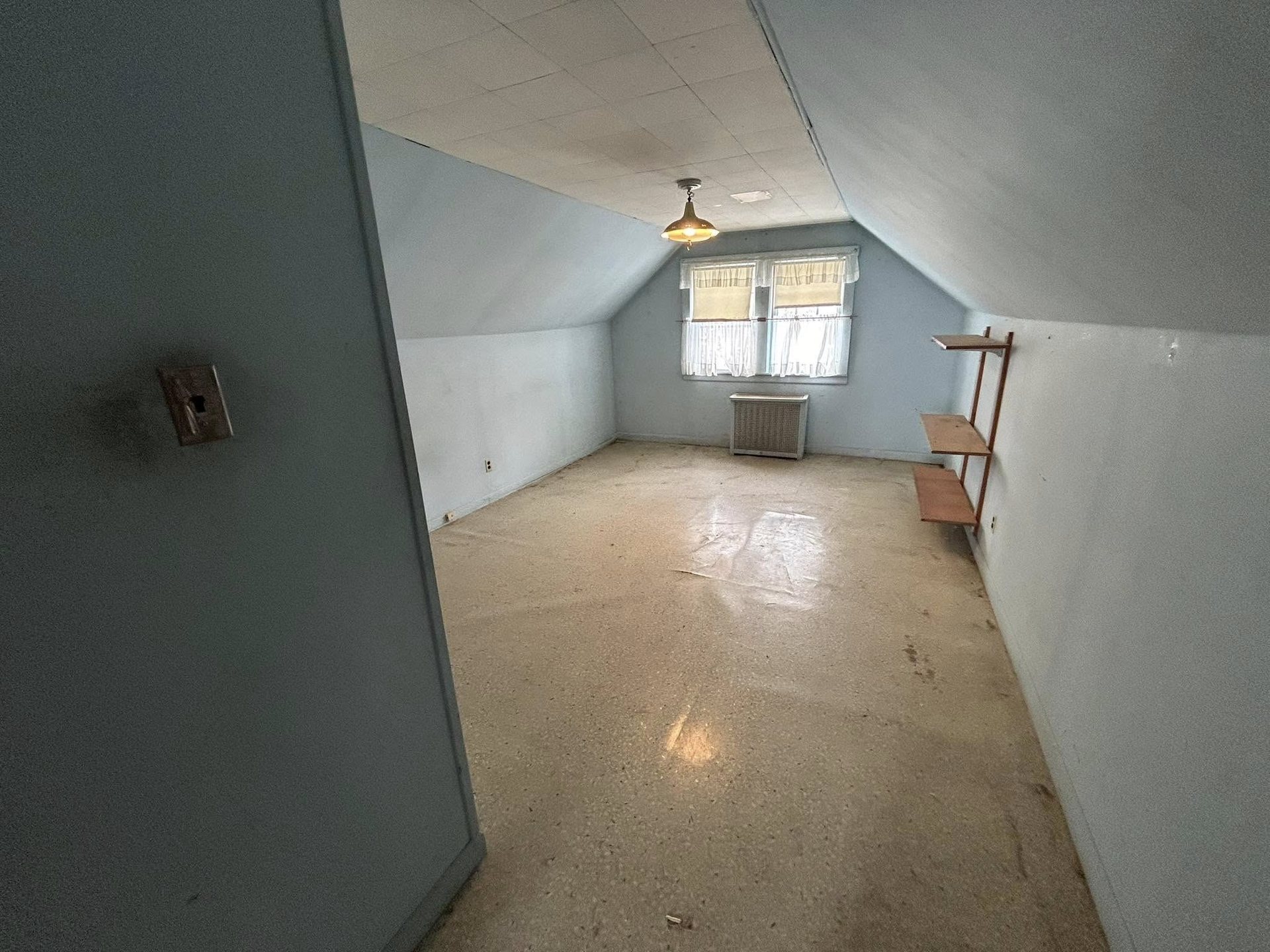 An empty room with a ceiling fan and two windows.