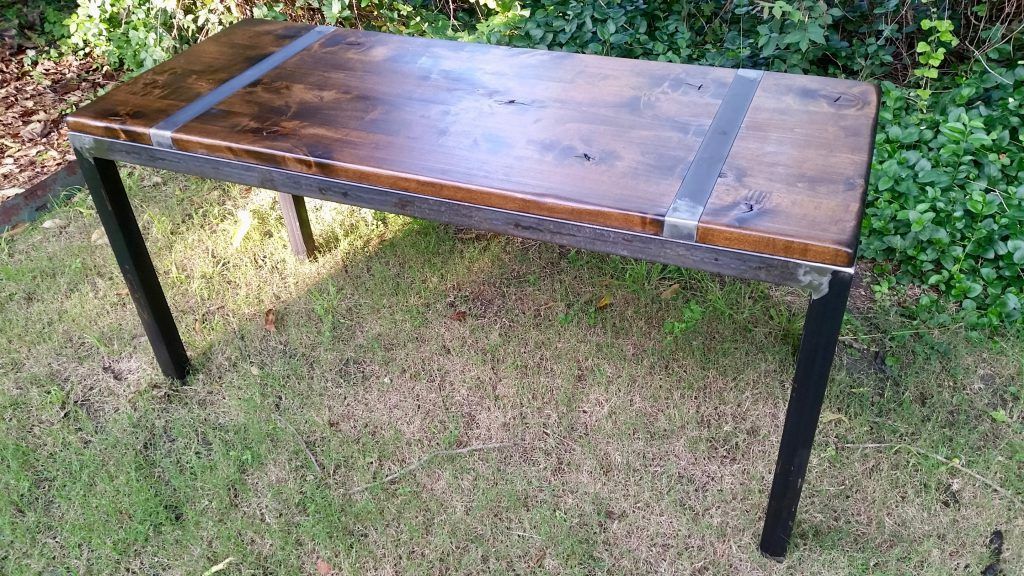 A wooden table with metal legs is sitting on top of a lush green field.