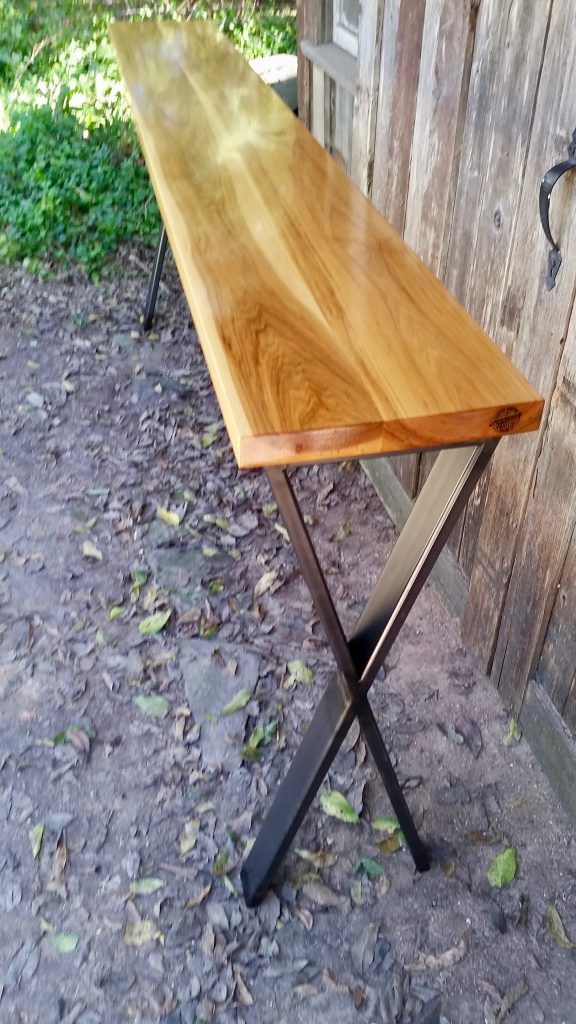 A wooden table with metal legs is sitting on the ground in front of a wooden building.