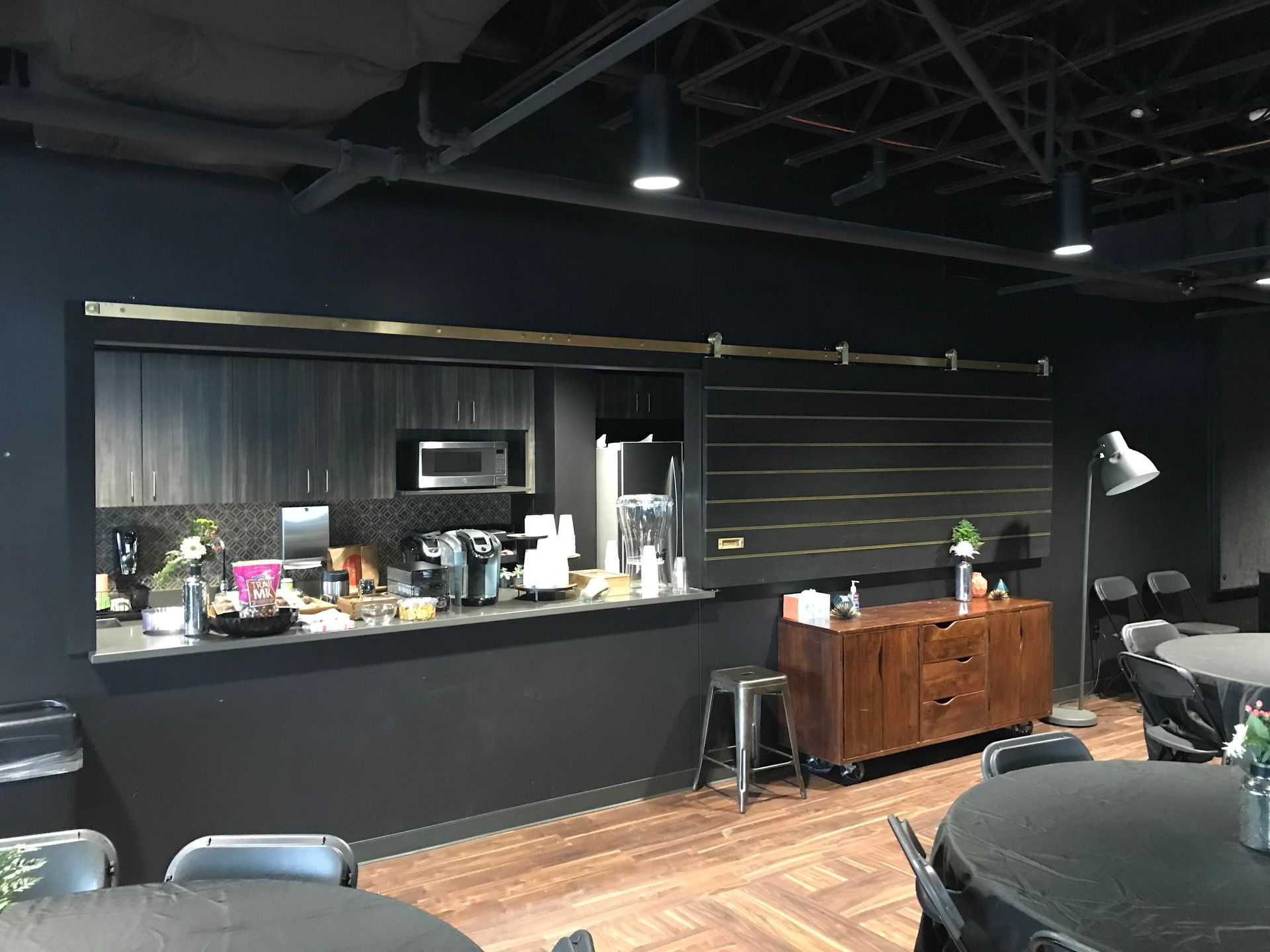 A room with tables and chairs and a kitchen in the background.