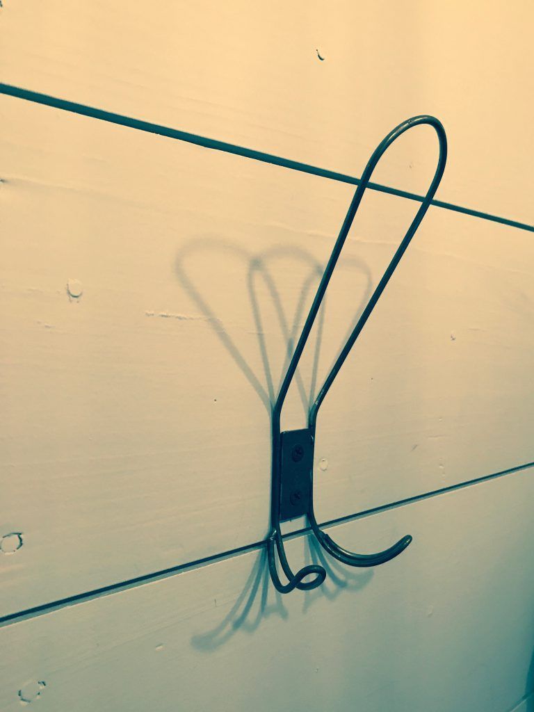 A shadow of a hook is cast on a white wall