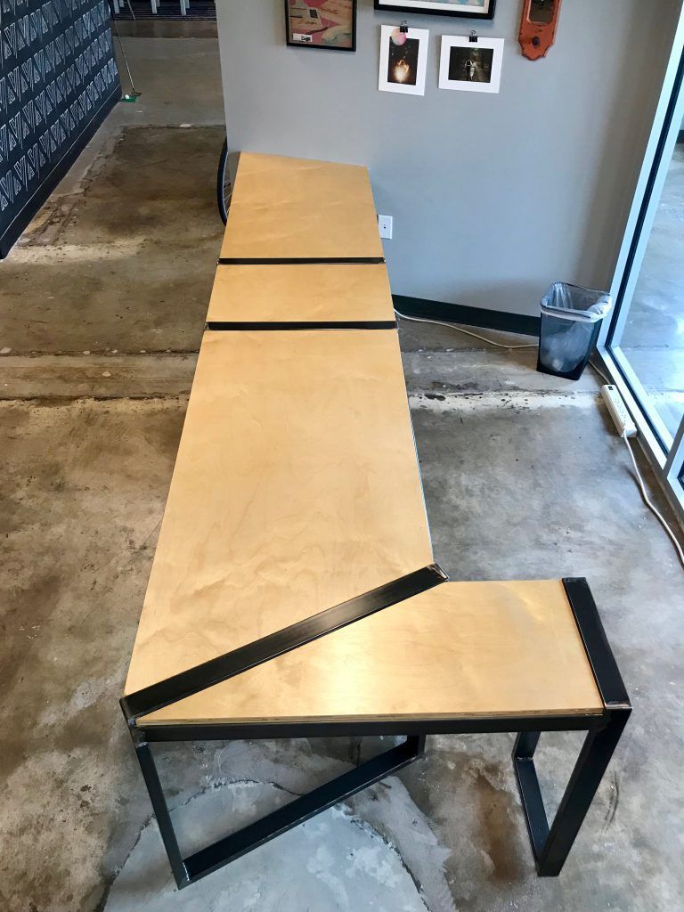 A long wooden table with a metal frame is sitting on a concrete floor in a room.