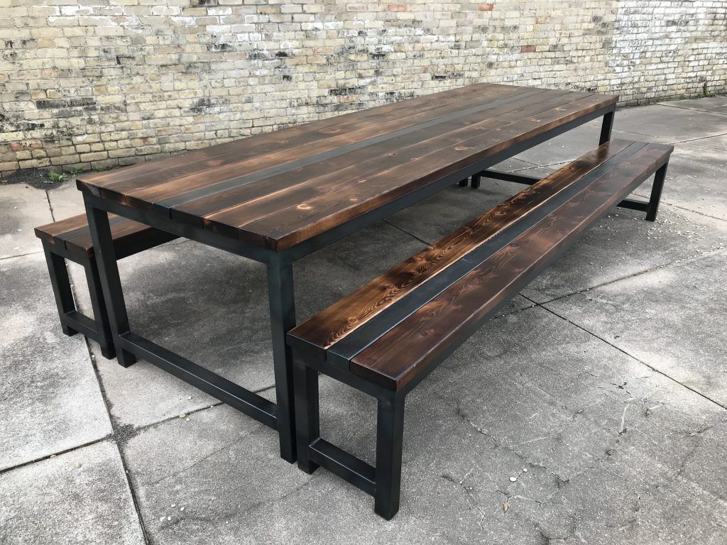 A wooden picnic table with two benches next to a brick wall.