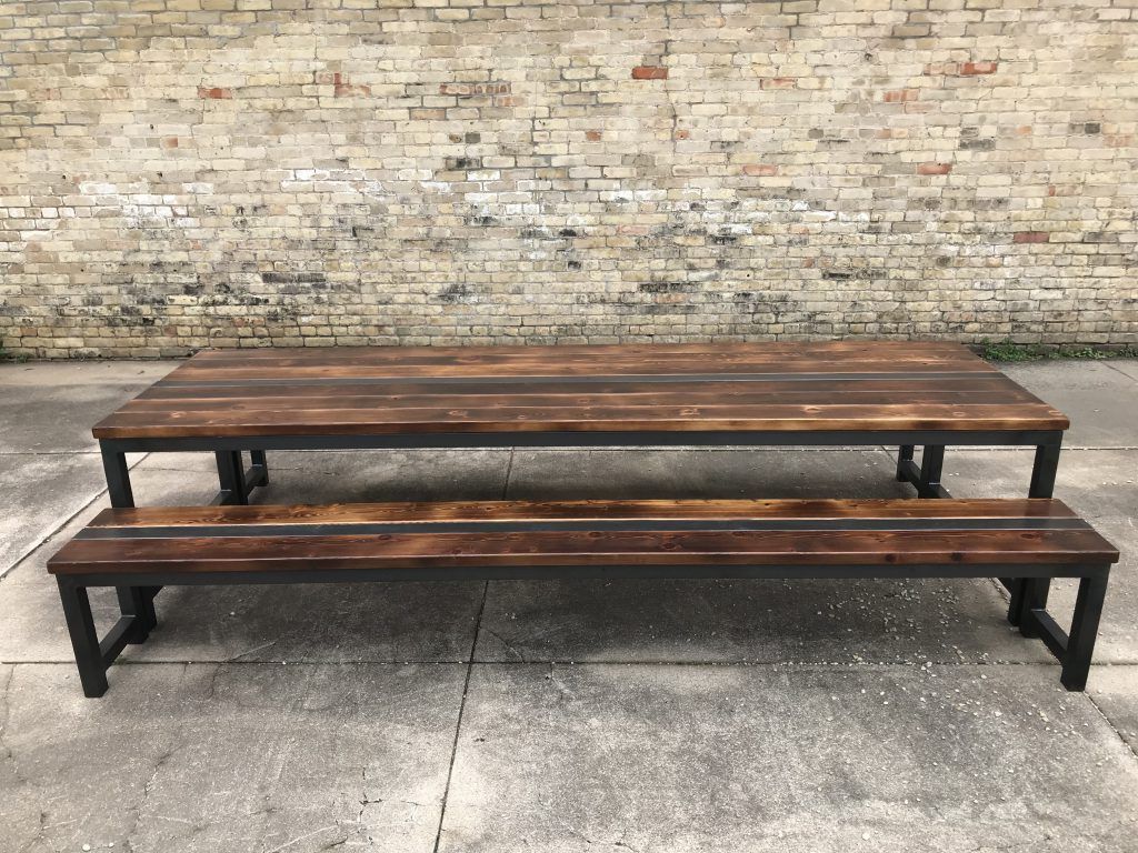 A wooden picnic table with two benches in front of a brick wall.
