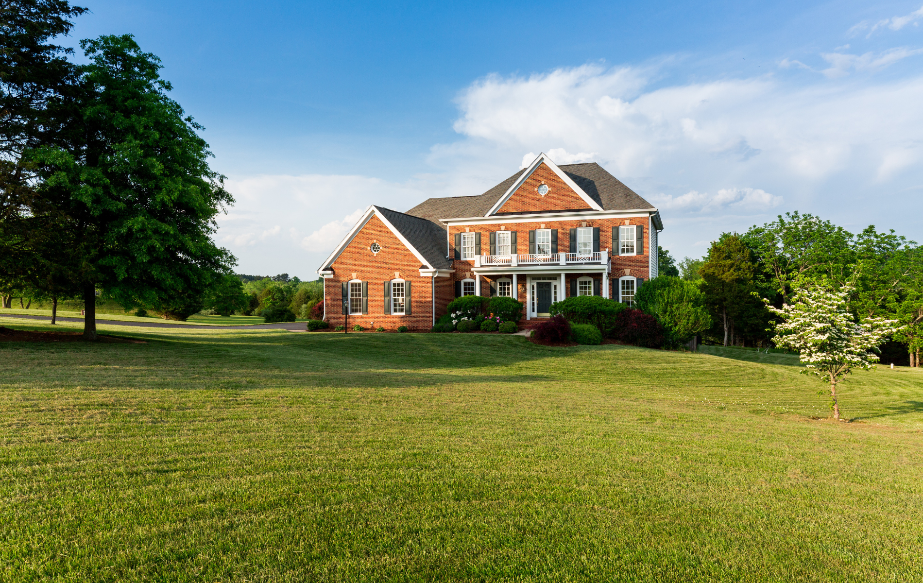 A large brick house is sitting in the middle of a lush green field.