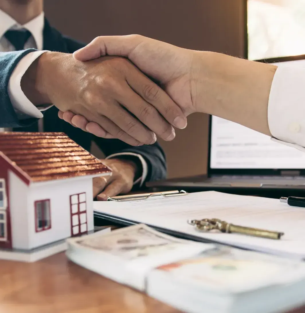 A man in a suit and tie is shaking hands with a woman in front of a model house.