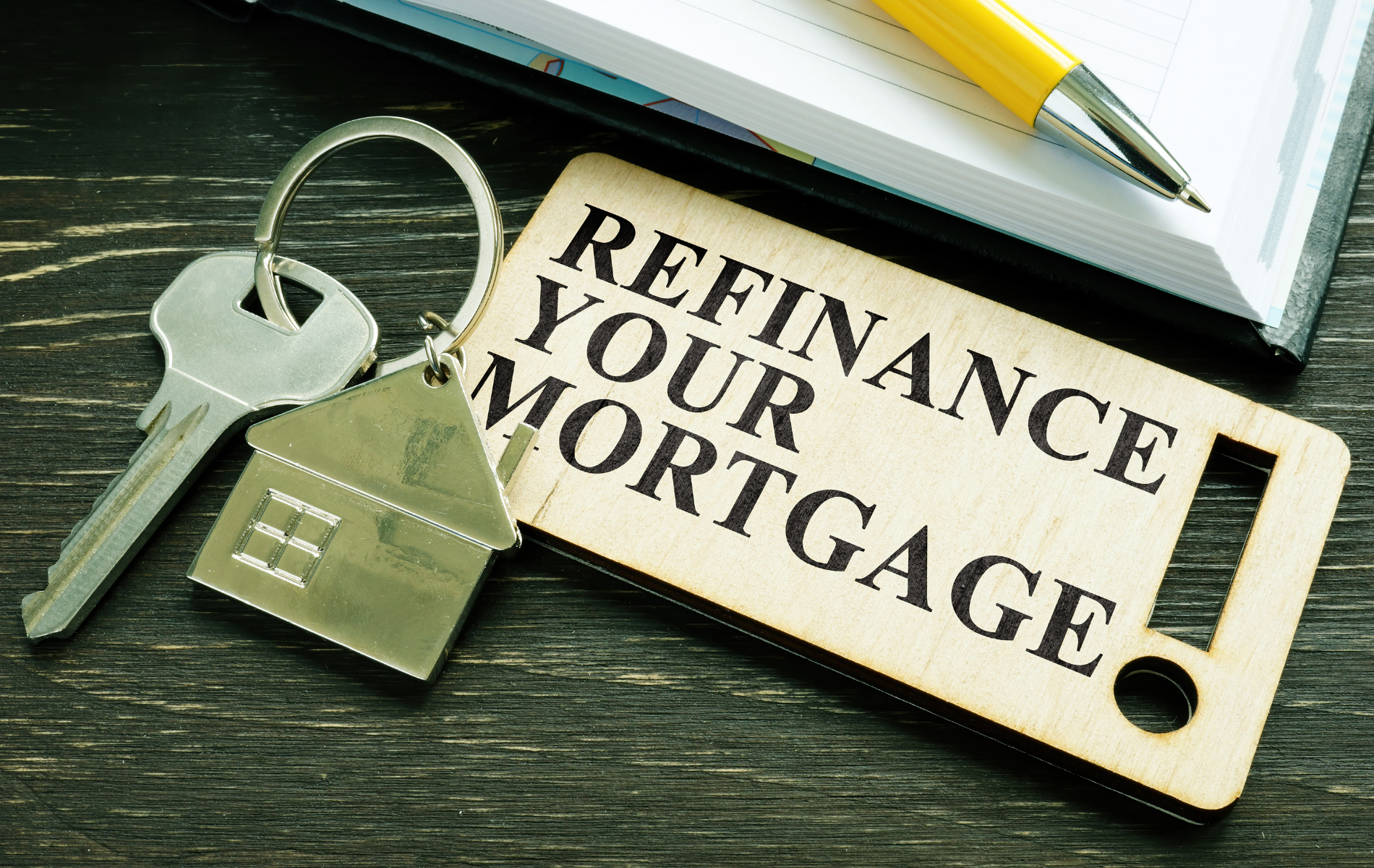 A pair of keys sitting next to a sign that says refinance your mortgage.