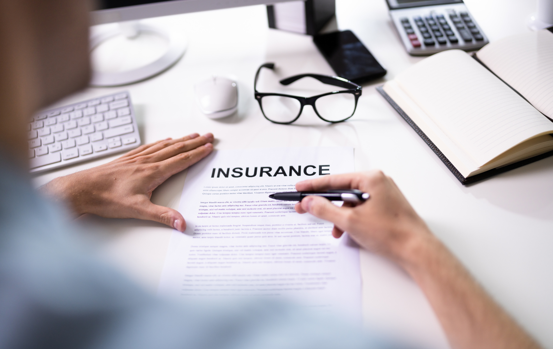 A man is sitting at a desk writing on a piece of paper that says insurance.