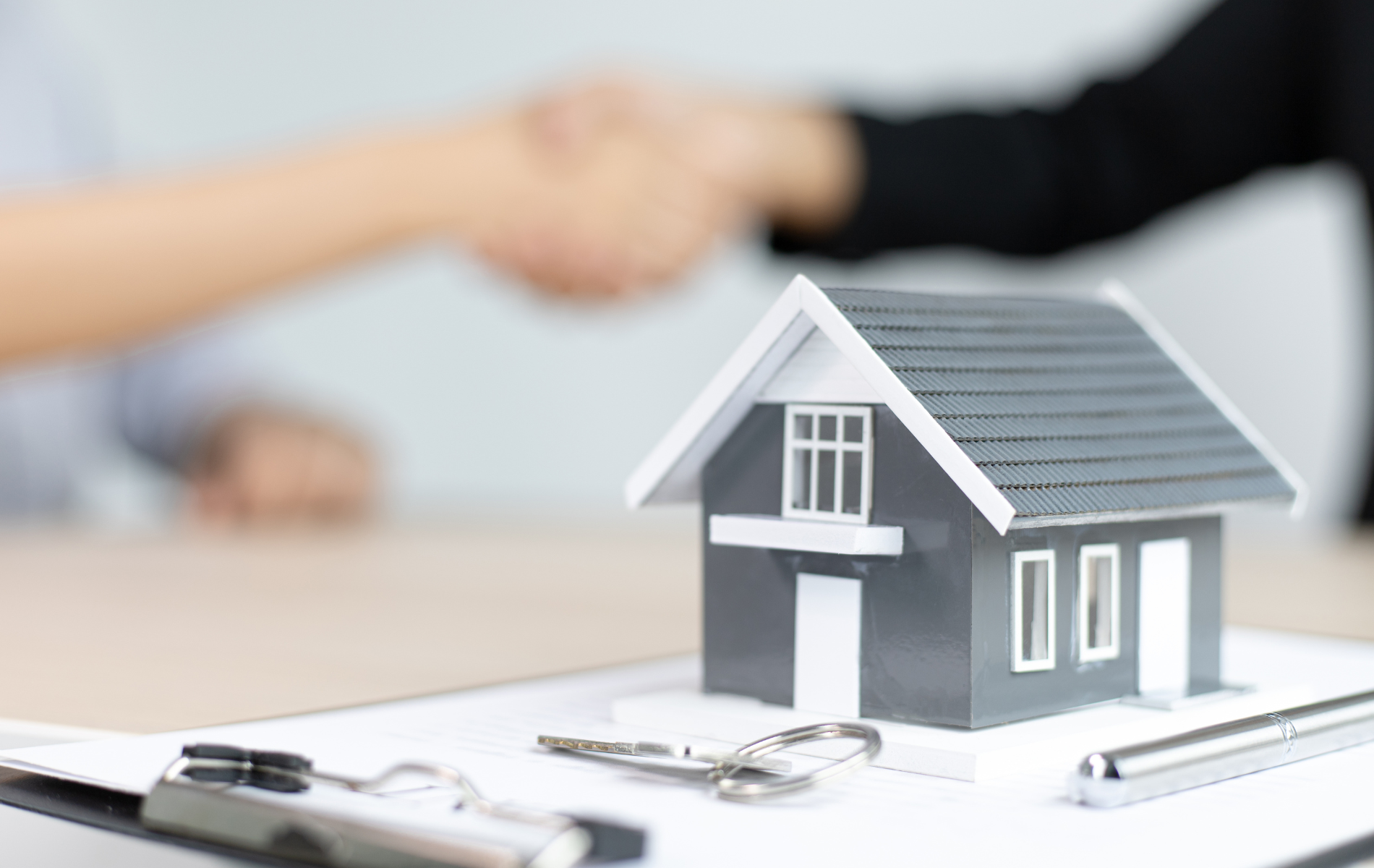 A person is shaking hands with a real estate agent in front of a model house.