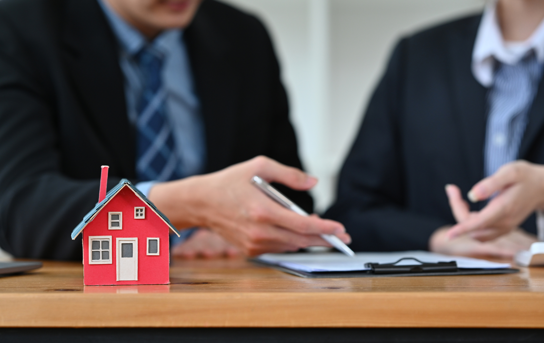 A man and a woman are sitting at a table with a model house and a pen.