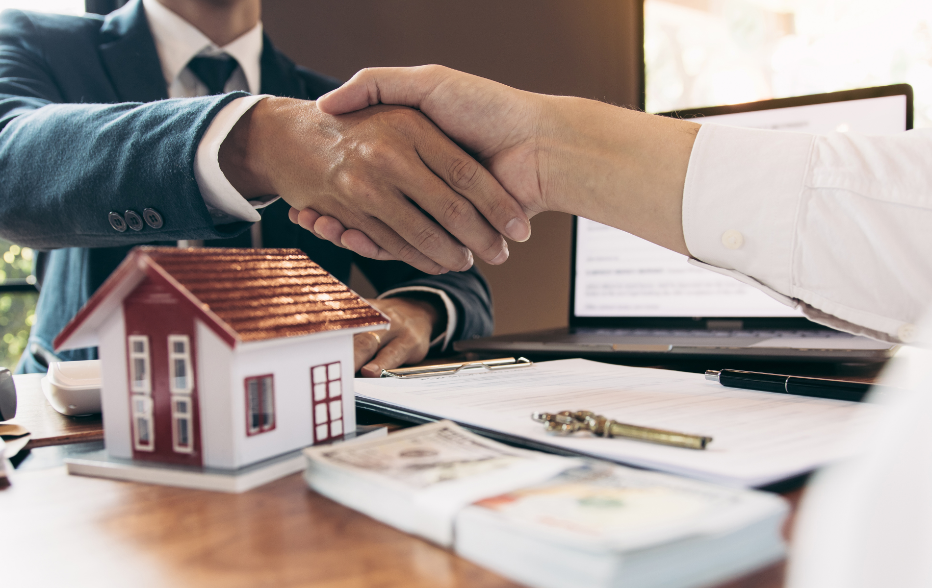 A man in a suit and tie is shaking hands with a woman in front of a model house.