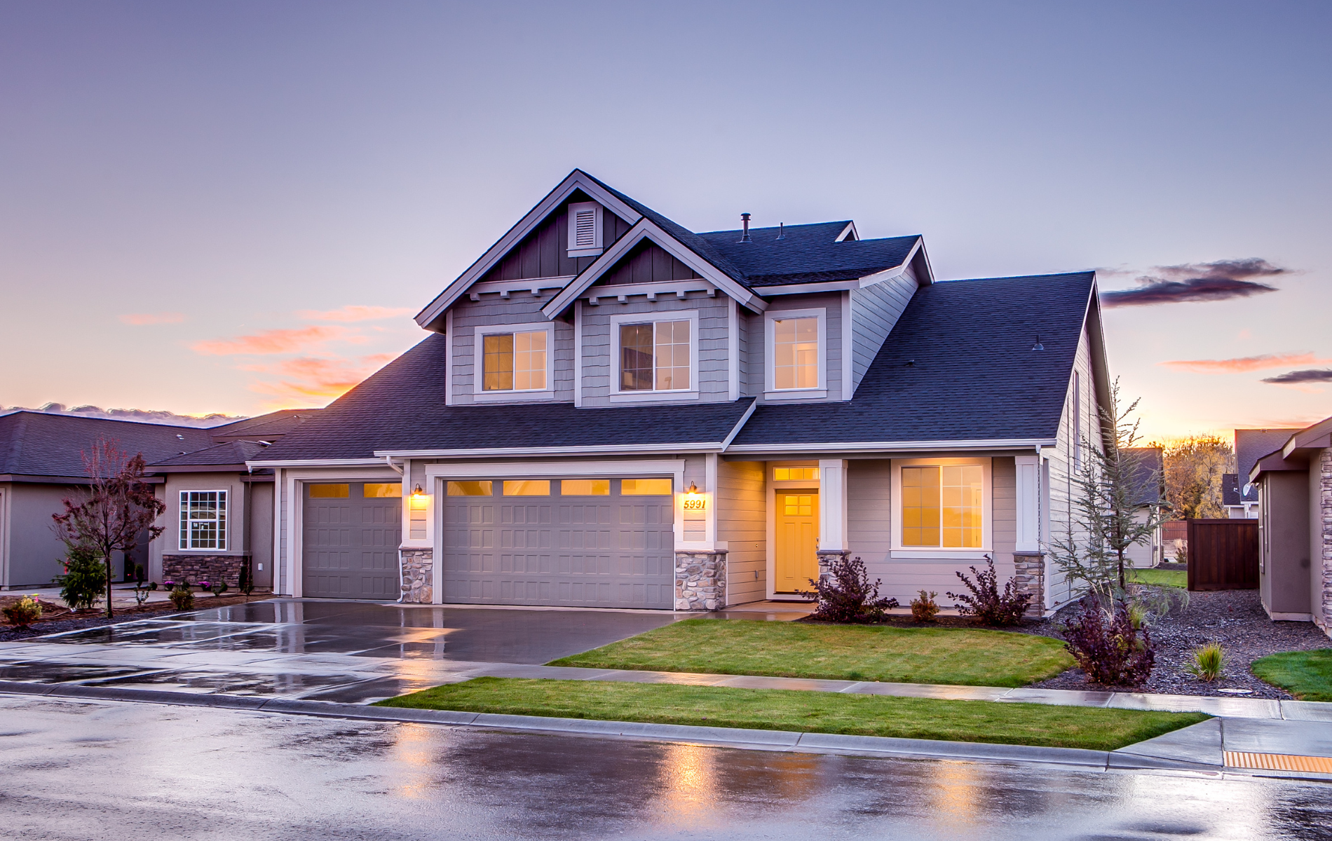 A large house with a garage and a driveway on a rainy day.