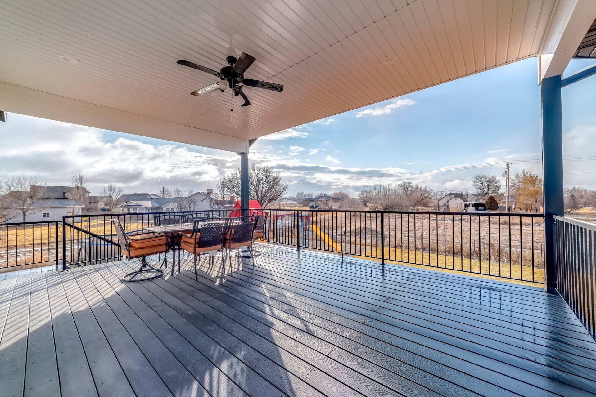 Covered deck with dark metal railings, outdoor furniture, and ceiling fan.