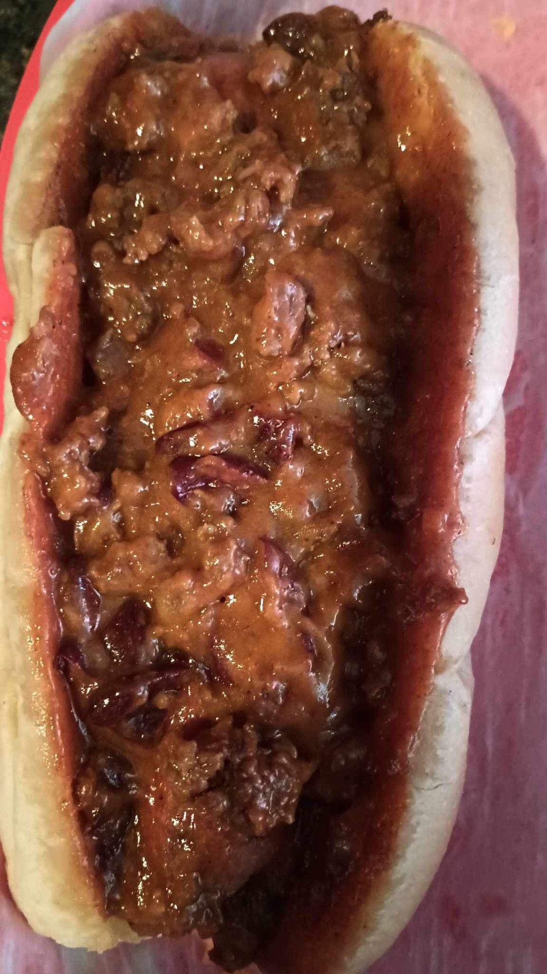 A close up of a chili dog on a bun on a plate.