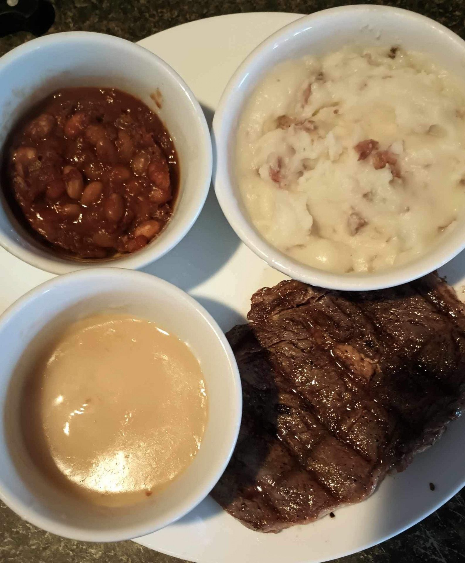 A plate of food with beans mashed potatoes and sauces