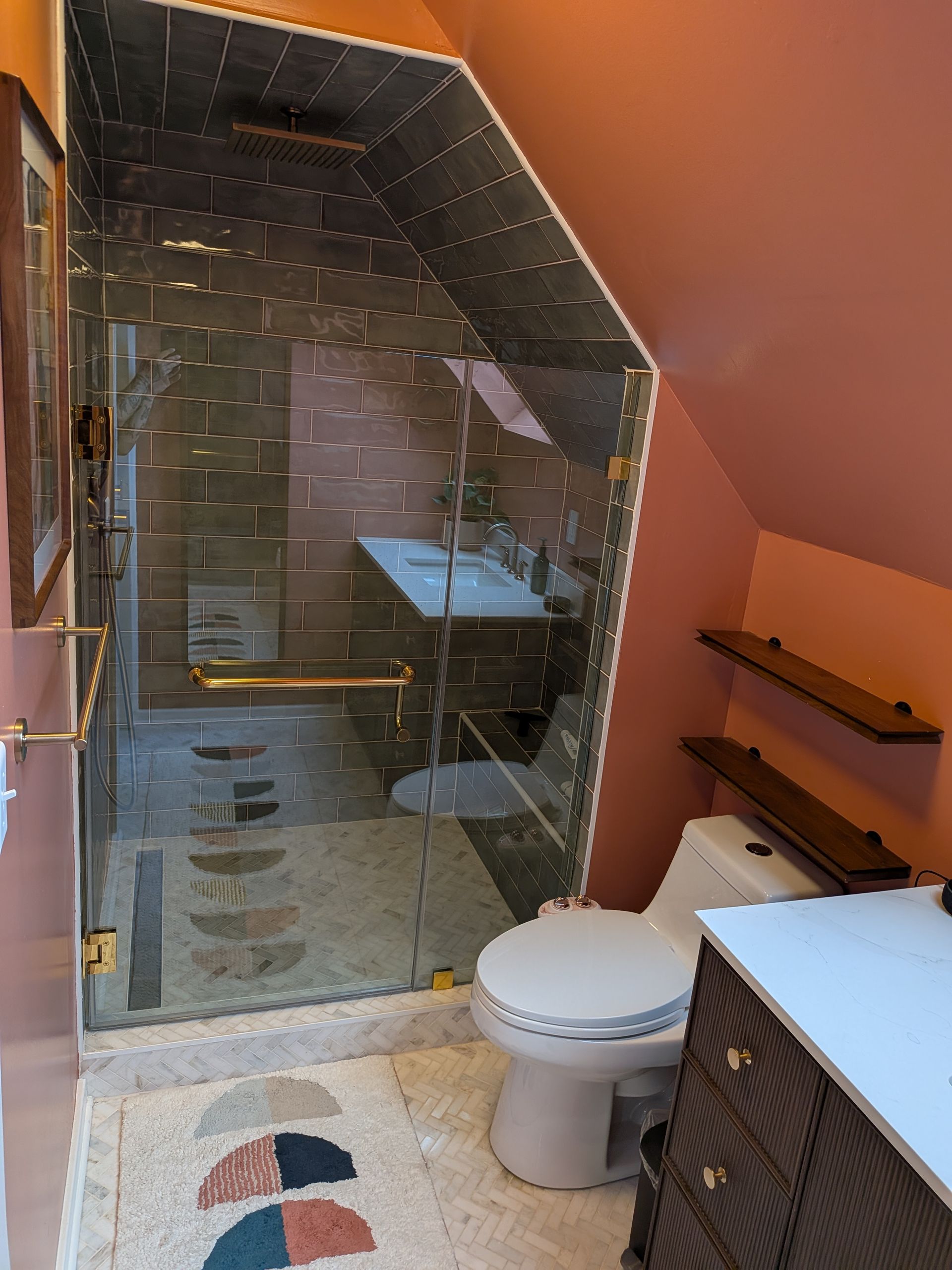 Bathroom with glass shower, toilet, and floating shelves against pink walls.