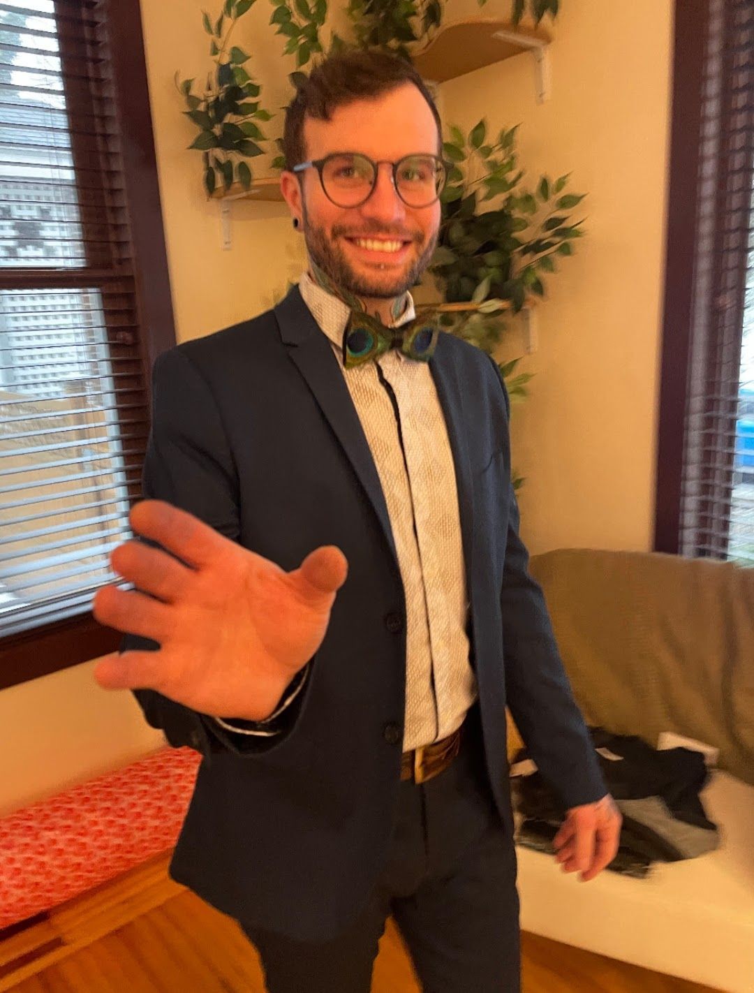 Man in blue suit, bow tie, and glasses, smiles and extends hand toward the viewer.