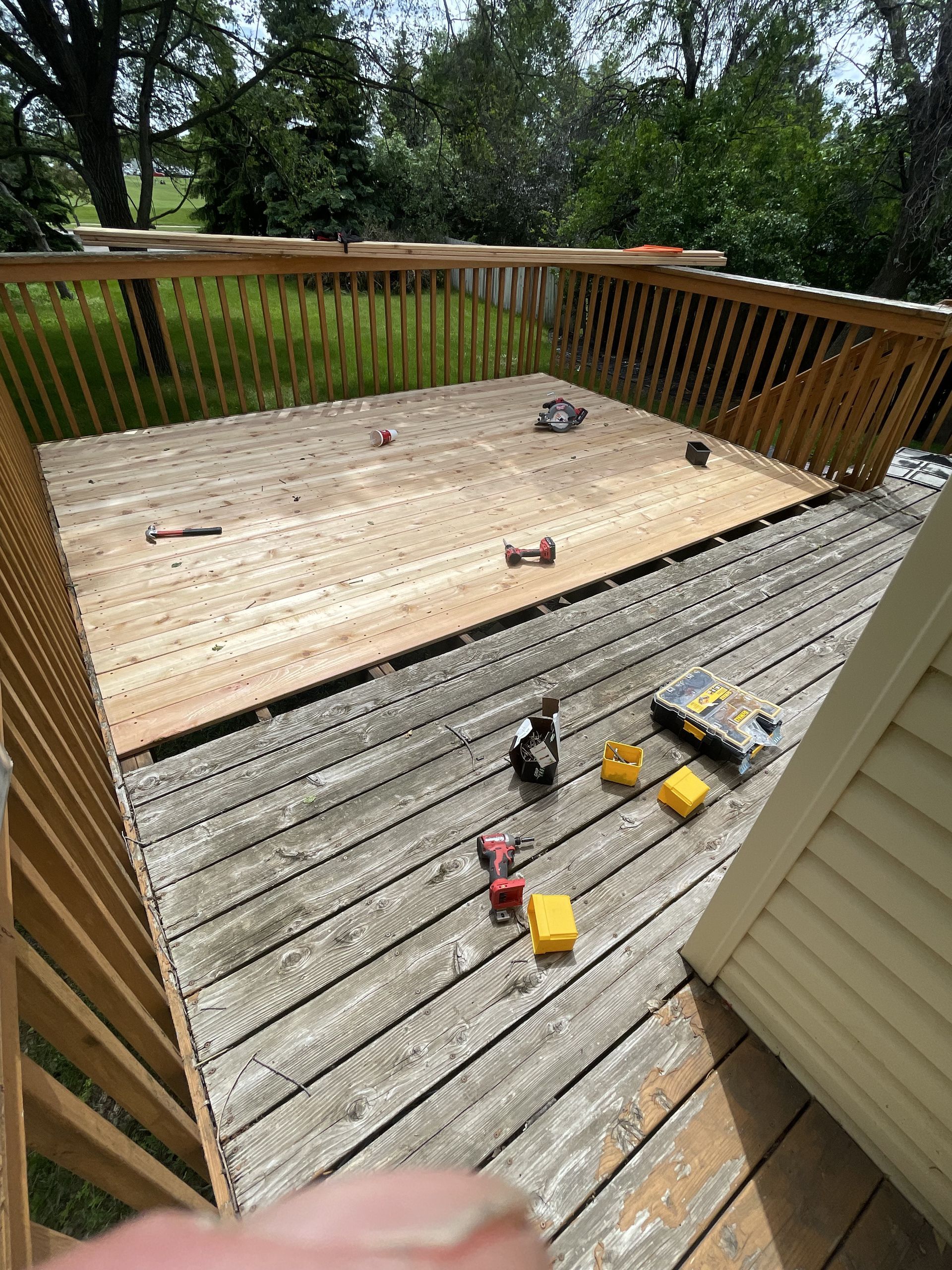 Wooden deck partially replaced, tools scattered, surrounded by railing, outdoors.