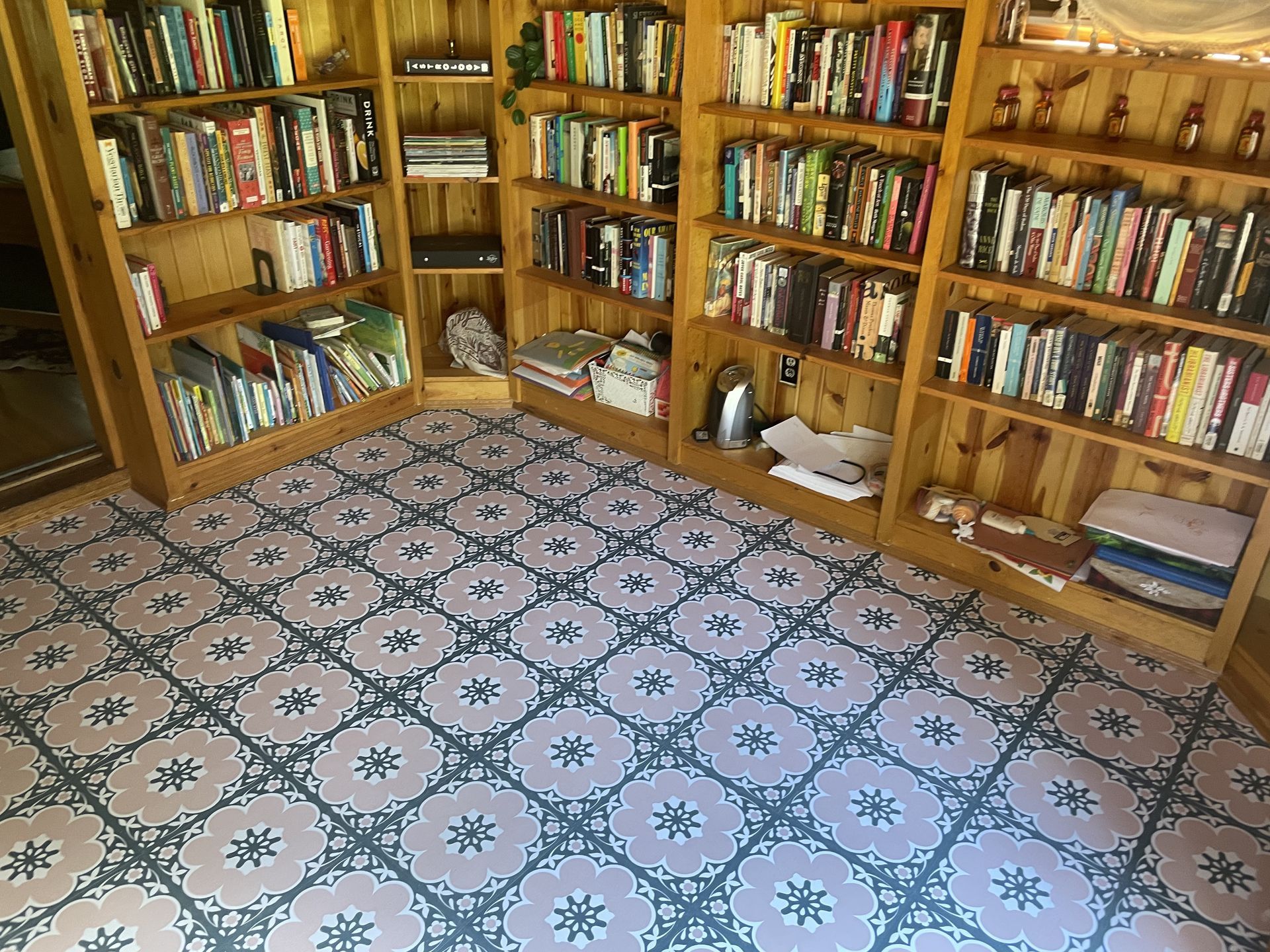 Bookshelves filled with books, sitting on a patterned floor. Wooden shelves in a corner of a room.