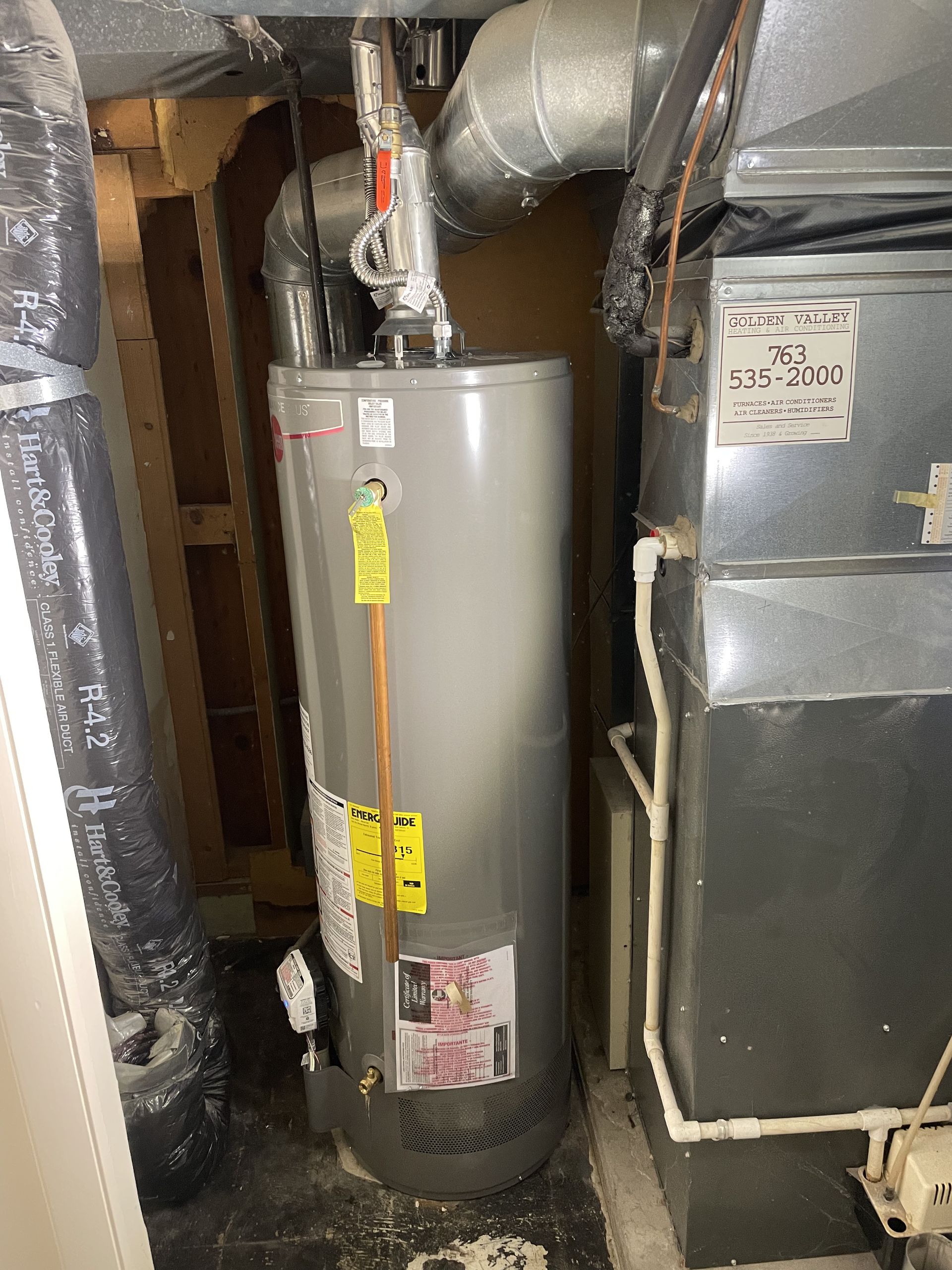 Water heater in a small utility room next to a furnace and ductwork.